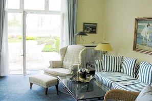 A living room with a sofa, armchair, and ottoman, a glass coffee table with a tray, a lamp, and a painting on the wall. - in Villa Fortuna by the sea - Apartment 1 (Bansin)