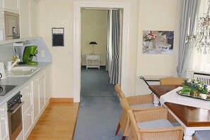 A kitchen with white cabinets, a green coffee maker, and a dining area with a wooden table and wicker chairs. - in Villa Fortuna by the sea - Apartment 1 (Bansin)