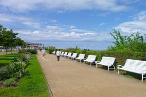 A pathway lined with white benches, a grassy area, and a building in the background. - in Villa Fortuna by the sea - Apartment 1 (Bansin)