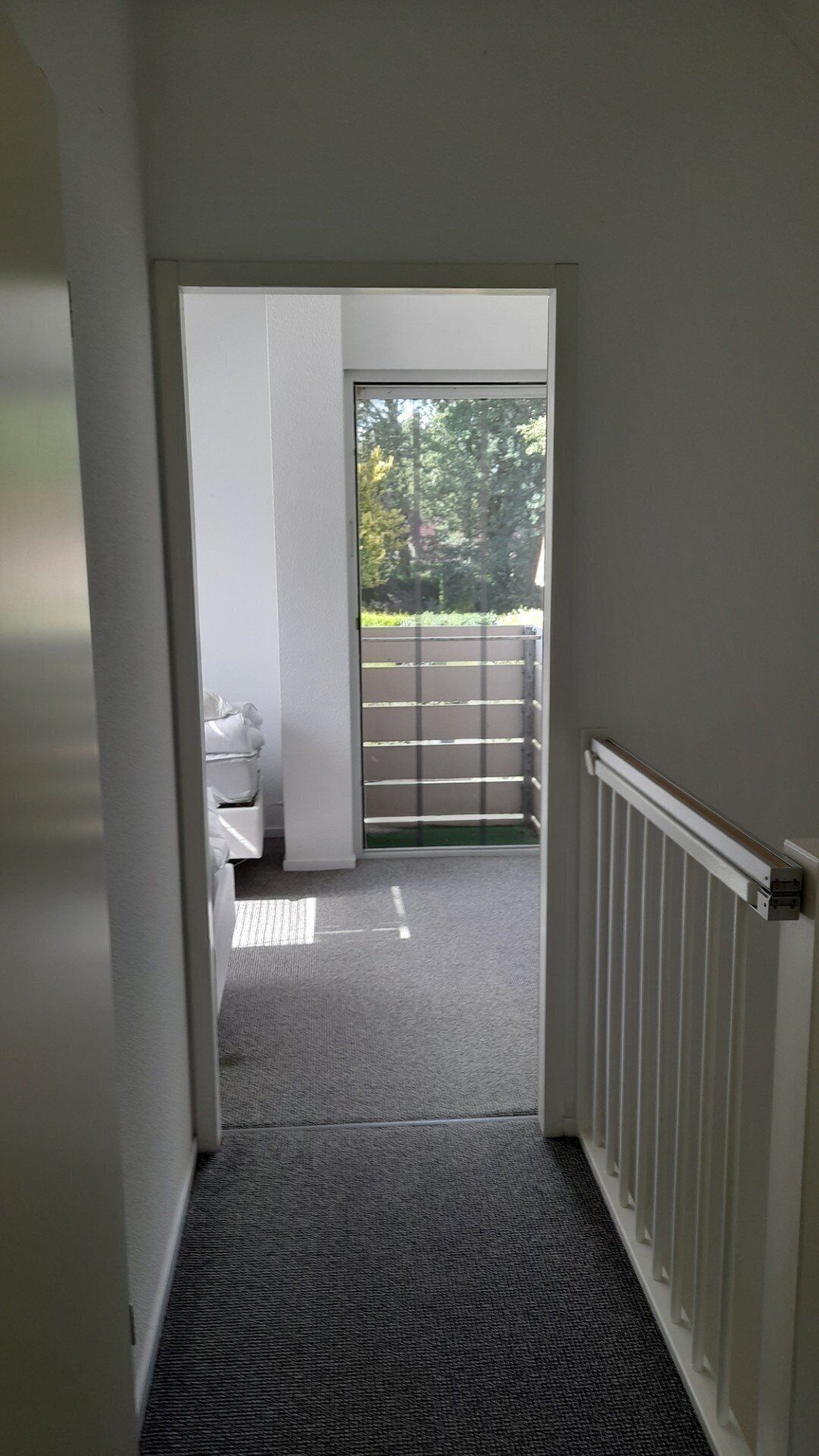 Een gang die uitkomt op een balkon met uitzicht op bomen en een hek.