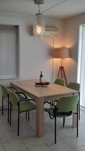 Een eetruimte met een houten tafel, groene stoelen, een fles wijn en een schaal fruit.