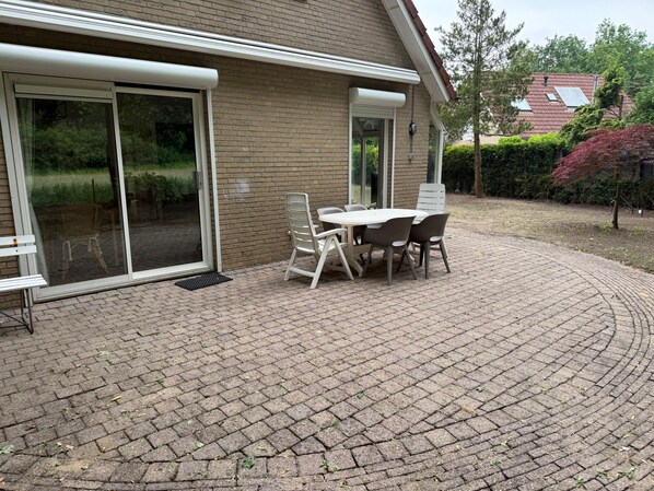 A patio with a table and chairs, a bench, and a sliding glass door leading to a garden.