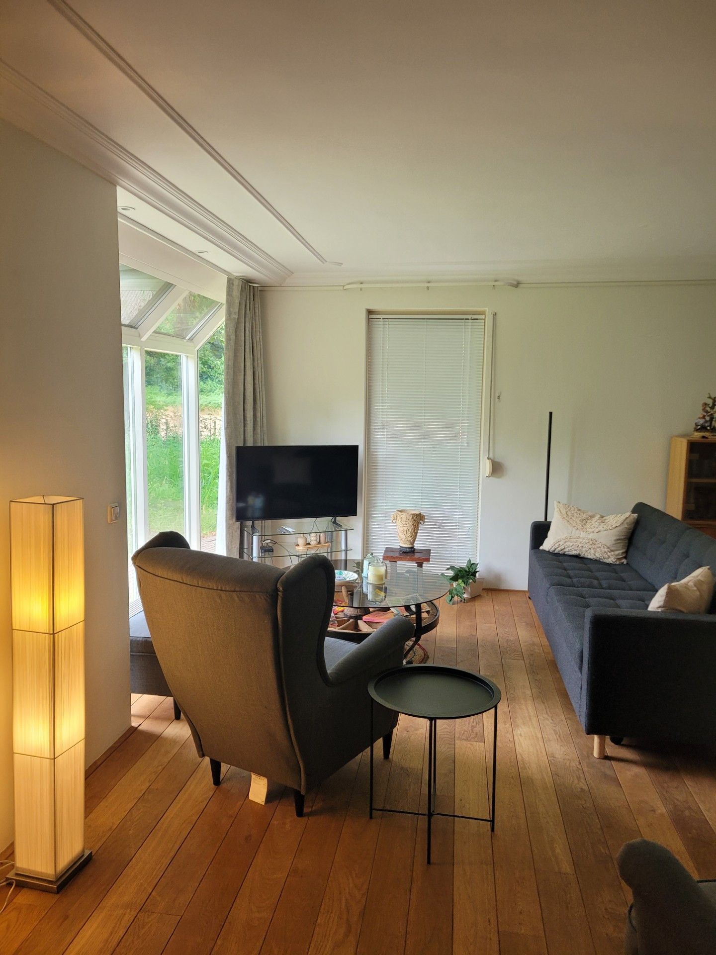 Un salon comprenant un canapé, un fauteuil, un téléviseur et une petite table avec une lampe.