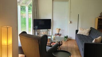 Un salon comprenant un canapé, un fauteuil, un téléviseur et une petite table avec une lampe.
