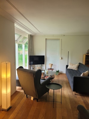 A living room with a sofa, armchair, TV, and a small table with a lamp.