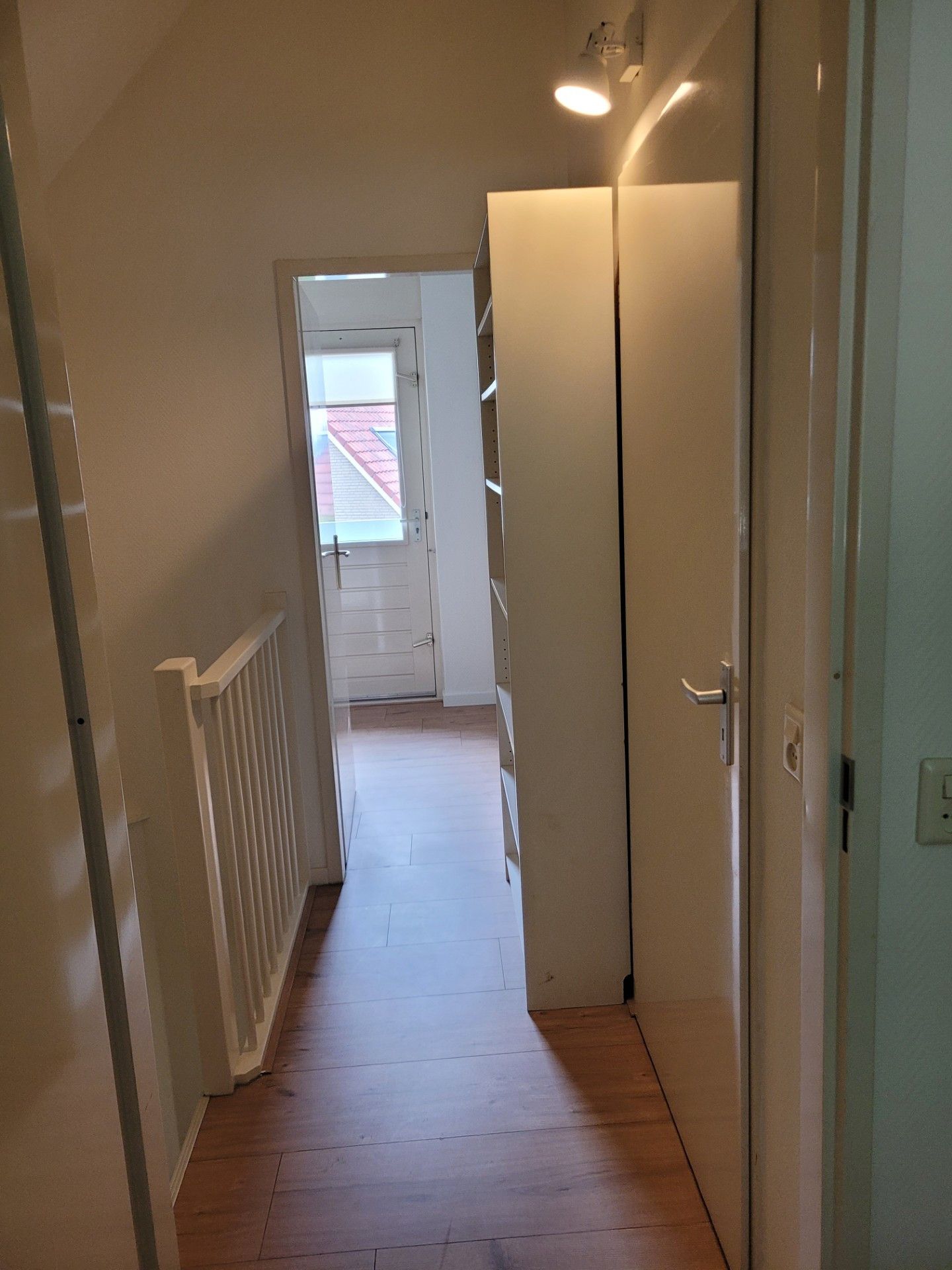 Un couloir étroit avec une porte donnant sur une pièce équipée d’un radiateur blanc et d’un luminaire au plafond.