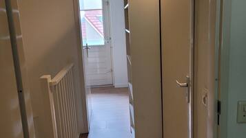 Un couloir étroit avec une porte donnant sur une pièce équipée d’un radiateur blanc et d’un luminaire au plafond.