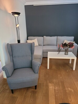 A living room with a grey armchair, a sofa, a white coffee table, and a floor lamp.