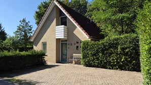 A single-story building with a sloped roof, a paved driveway, and a bench in front. - Wighenerhorst Bungalow Park - 49 (Wijchen)