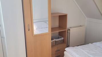 Une chambre avec une armoire en bois, un lit recouvert d’une couette blanche et un radiateur.