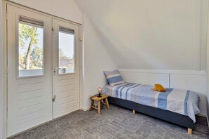 A small, single-bed room with a sloped ceiling, a window, and a door.