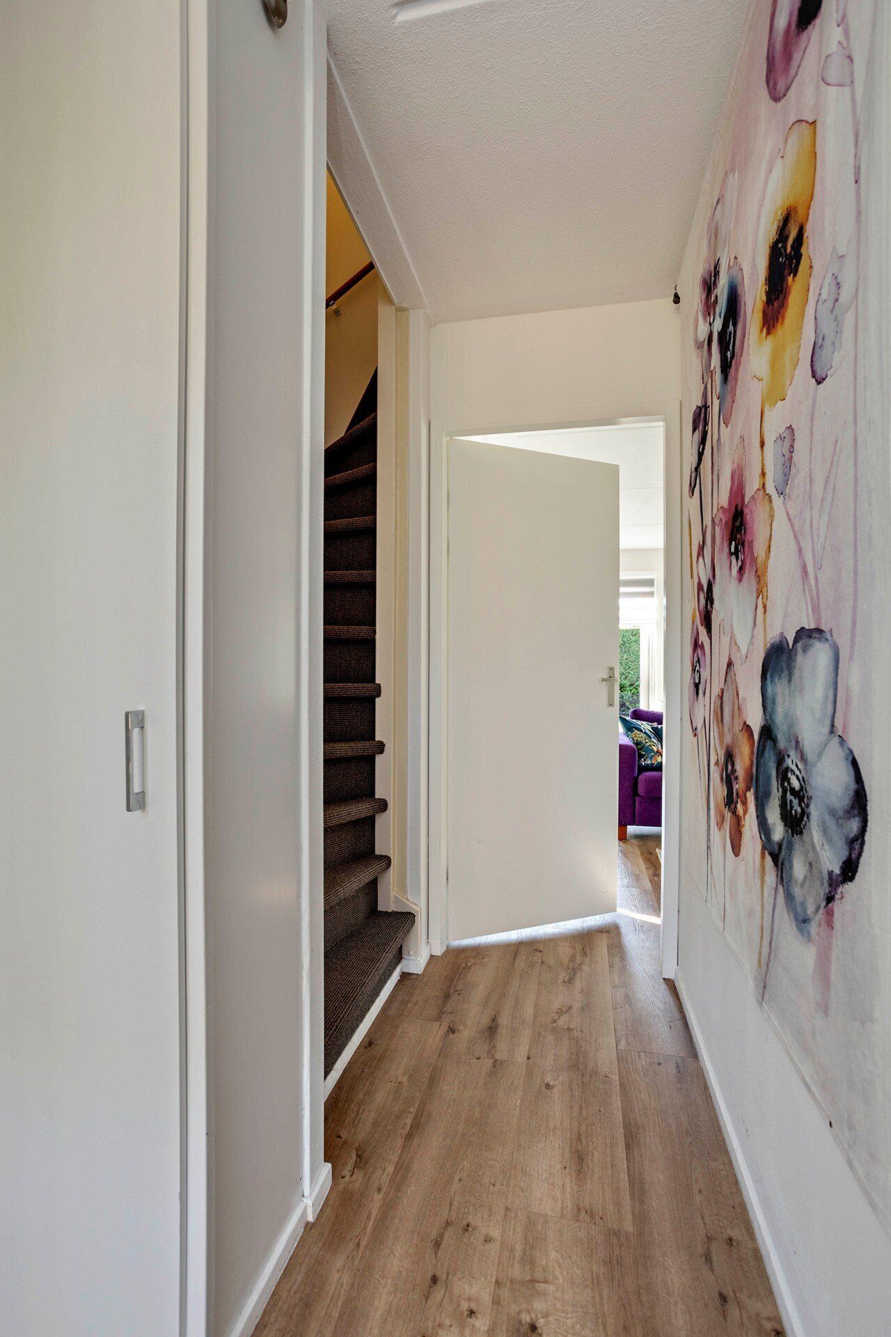 Ein Korridor mit Holzboden, einer Treppe und einer Wand mit einem floralen Gemälde.