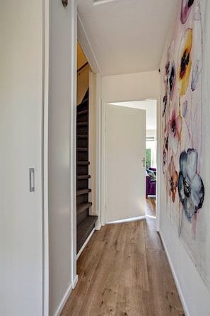 Een hal met houten vloer, een trap en een wand met een bloemschilderij.