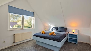 Ein Schlafzimmer mit schrägem Dach, einem großen Bett, einem Fenster mit Aussicht, einem Heizkörper und Nachttischlampen.
