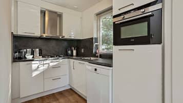 Una cocina moderna con armarios blancos, una campana de acero inoxidable, horno empotrado y lavavajillas.