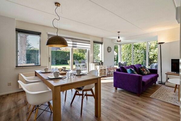 A spacious living area with a dining table, a purple sofa, and a television.