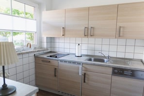 Een keuken met lichte houten kastjes, een RVS spoelbak en een vaatwasser.