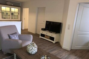 Ein Wohnzimmer mit einer Couch, einem Couchtisch, einem Fernseher auf einem Schrank und einer Vitrine.