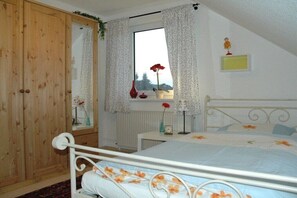 A bedroom with a bed, a wooden wardrobe, a window with curtains, and a radiator. - Holiday apartment with 2 bedrooms (Grünendeich)
