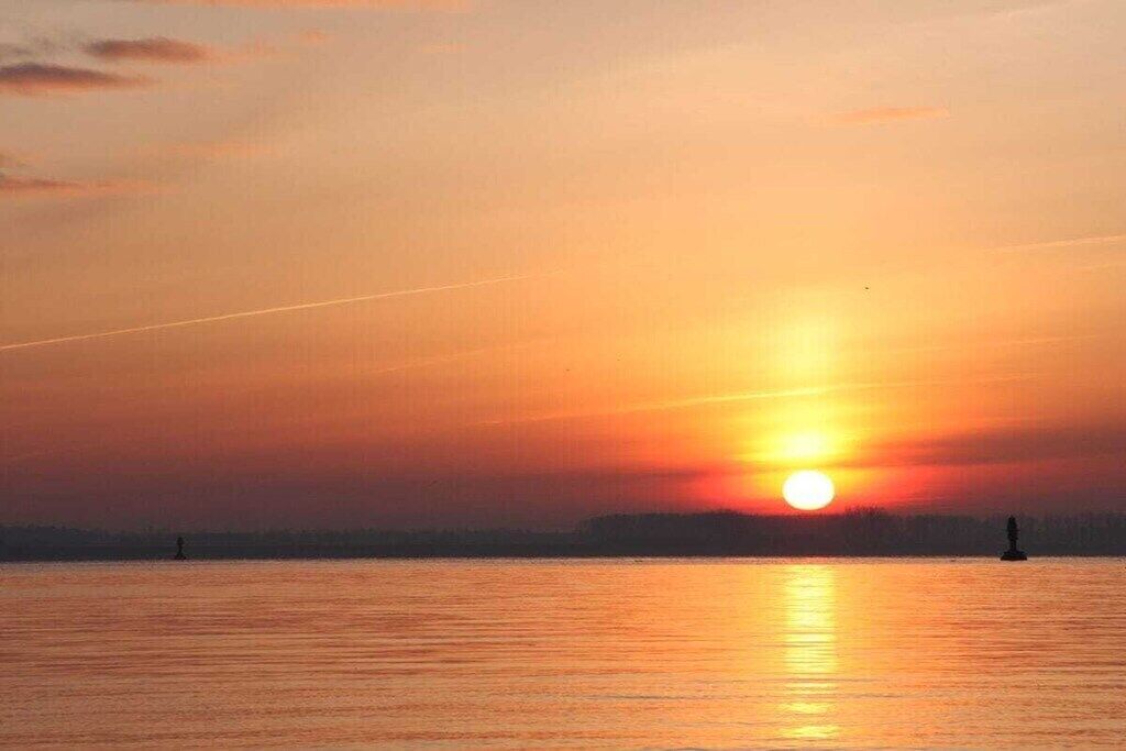 Un tramonto su acque calme, con la sagoma di una boa all'orizzonte.