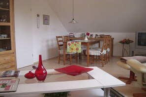 A dining area with a table, chairs, and a red vase on a white table. - Holiday apartment with 2 bedrooms (Grünendeich)
