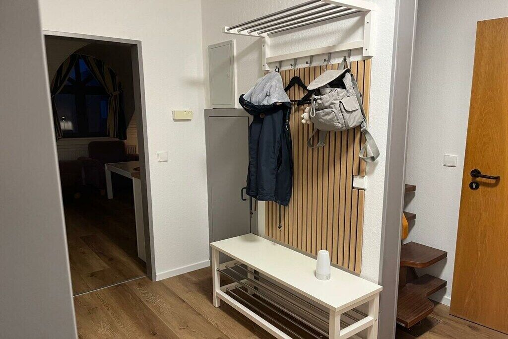 Un couloir avec un porte-manteau, un banc blanc et une porte.