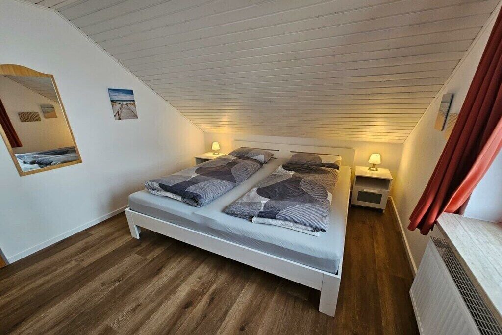 Ein Schlafzimmer mit Bett, Nachttischen, einem Spiegel und einem Fenster.