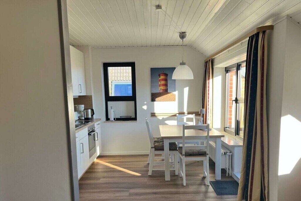 Een compacte keuken met witte kastjes, een eettafel met stoelen en een hangende hanglamp.