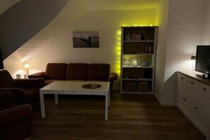 A cozy living room with a white coffee table, brown sofa, and a bookshelf. - Holiday apartment 3 House Froschblick (Greetsiel)