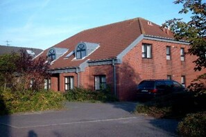 A red brick building with a pitched roof and a garage door. - Holiday apartment 3 House Froschblick (Greetsiel)