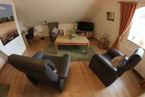 A cozy living room with a wooden coffee table, two black sofas, a striped armchair, a television, and a painting on the wall. - Holiday apartment with 1 bedroom (Bremen)