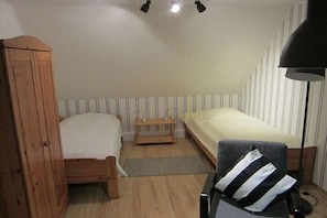 Un piccolo alloggio in un'unica stanza, con un'armadietto di legno, un letto con materasso bianco, un comodino e una lampada.