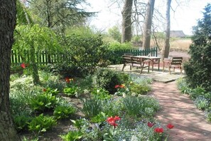 Un giardino con vialetto lastricato, panchine in legno e diverse piante e fiori.