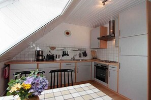 A kitchen with white cabinets, a stove, a sink, and a dining table with chairs. - Holiday apartment with 1 bedroom (Bremen)
