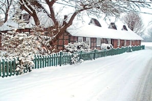Una casa con tetto innevato, recinzione verde e facciata in mattoni.