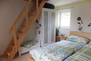 Un dormitorio con escalera de madera, un armario, una mesita de noche con lámpara y ventana con vistas.