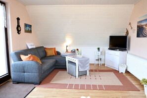 A living room with a grey sofa, a small white table, a TV, and a radiator. - Holiday apartment with 1 bedroom (Prerow)