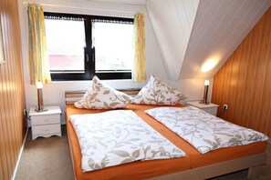 A bedroom with a bed, two bedside tables, a window with curtains, and a wooden ceiling. - Holiday apartment with 1 bedroom (Prerow)
