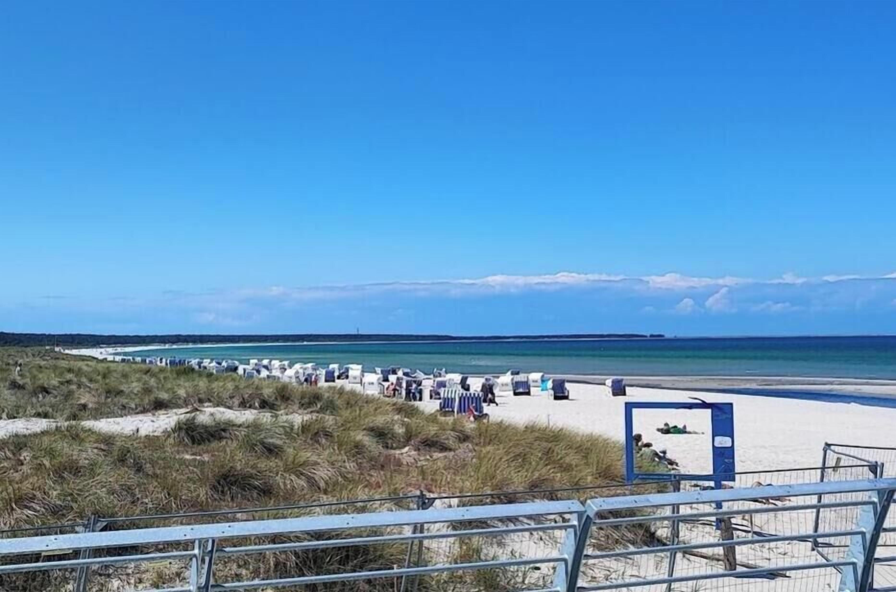 Une plage avec un ciel dégagé, un rivage sablonneux et quelques personnes.