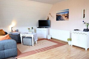 Una sala de estar amoblada con televisión, gabinetes blancos, un sofá y una pequeña mesa.