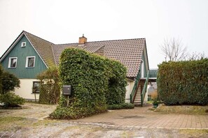 A two-story house with a green exterior, a tiled roof, and a brick pathway leading to the entrance. - Holiday apartment with 1 bedroom (Prerow)