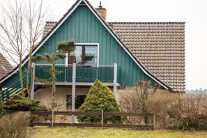 Una casa verde con balcón, rodeada de árboles y una valla de madera.