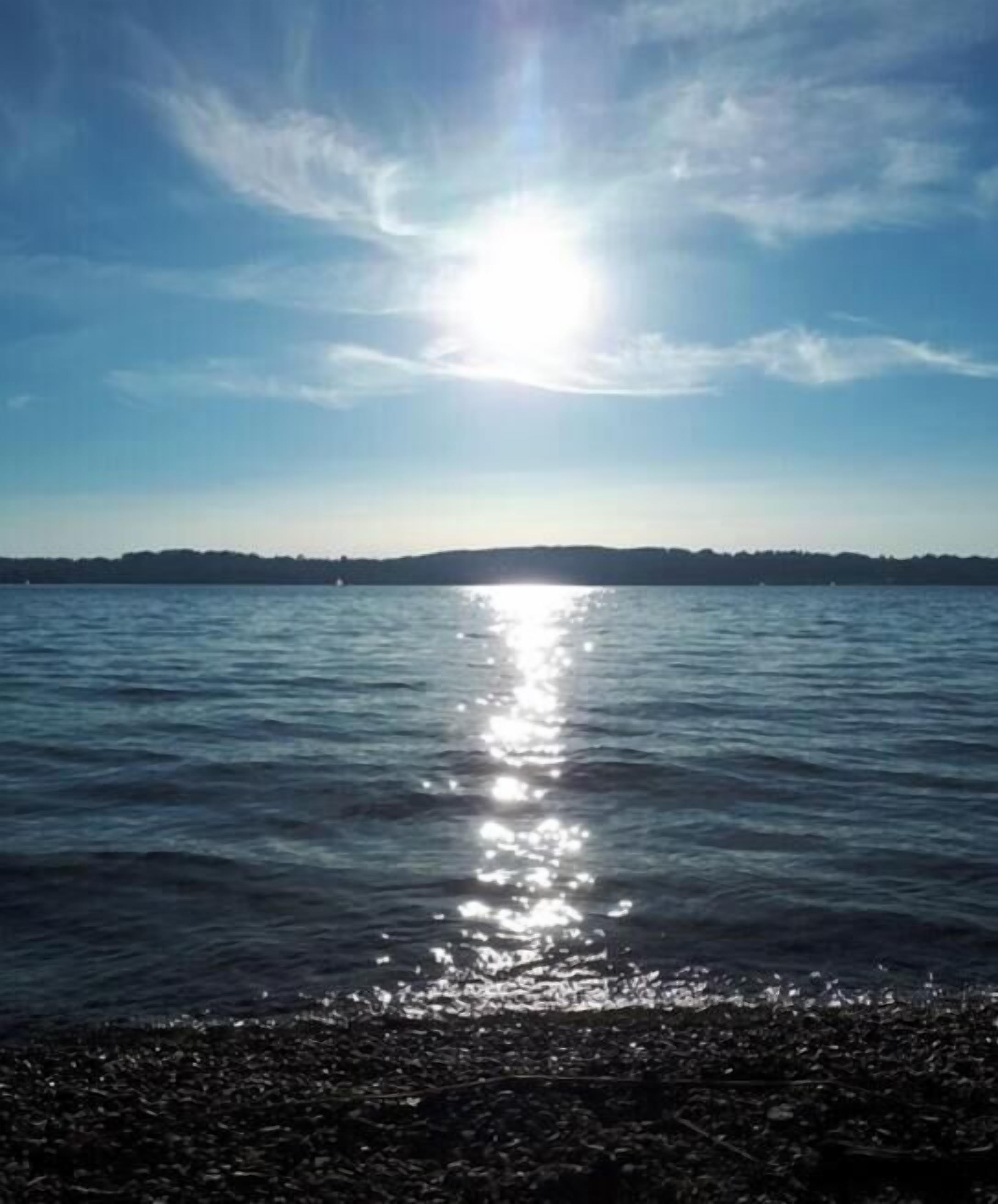 A calm body of water reflecting sunlight with a distant shoreline.