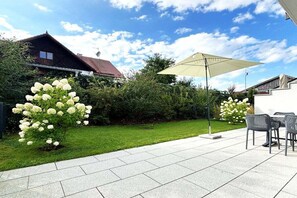 An outdoor patio area with a tiled floor, a table with chairs, and a large umbrella providing shade. - Holiday apartment with 2 bedrooms (Tutzing)