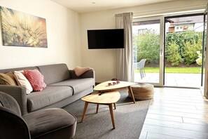 En moderne stue med sofa, sofabord og et fladskærms-tv ophængt på væggen.