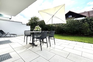 An outdoor patio with a table and chairs, a large umbrella, and a flower arrangement.