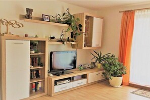 A living room with a flat-screen TV, wooden shelves, a potted plant, and a window with curtains. - Holiday apartment with 2 bedrooms (Zingst)