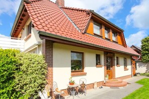 A two-story house with a red-tiled roof, a brick facade, and a small front porch with a table and chairs. - Holiday apartment with 2 bedrooms (Zingst)