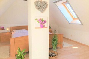 A bedroom with a sloped ceiling, a bed, a nightstand, a wall-mounted shelf with a picture, a potted plant, and a skylight. - Holiday apartment with 2 bedrooms (Zingst)