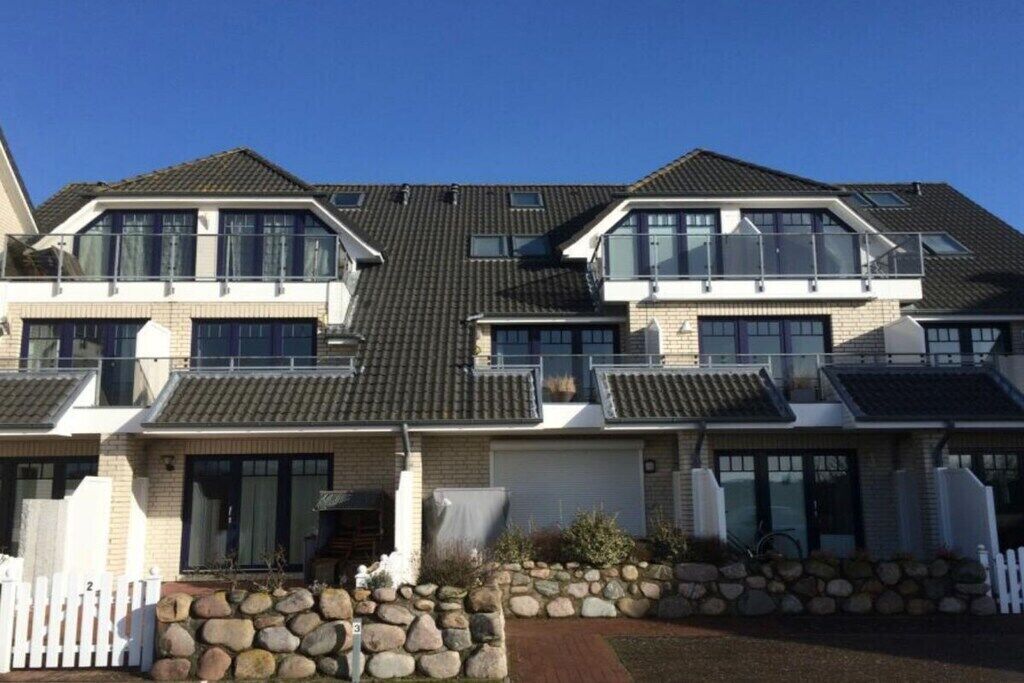 A two-story residential building with a tiled roof, large windows, and a stone foundation.